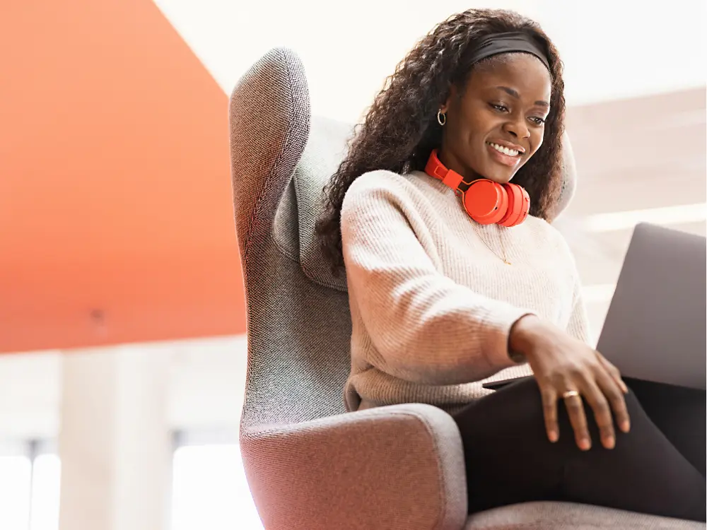 A Henkel employee sits in a comfy chair with her laptop on her knees. She smiles.