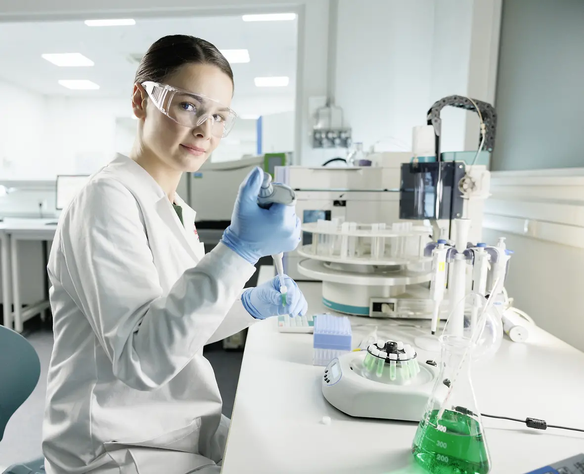 Eine Wissenschaftlerin experimentiert im Labor und trägt dabei einen Laborkittel sowie eine Sicherheitsbrille.