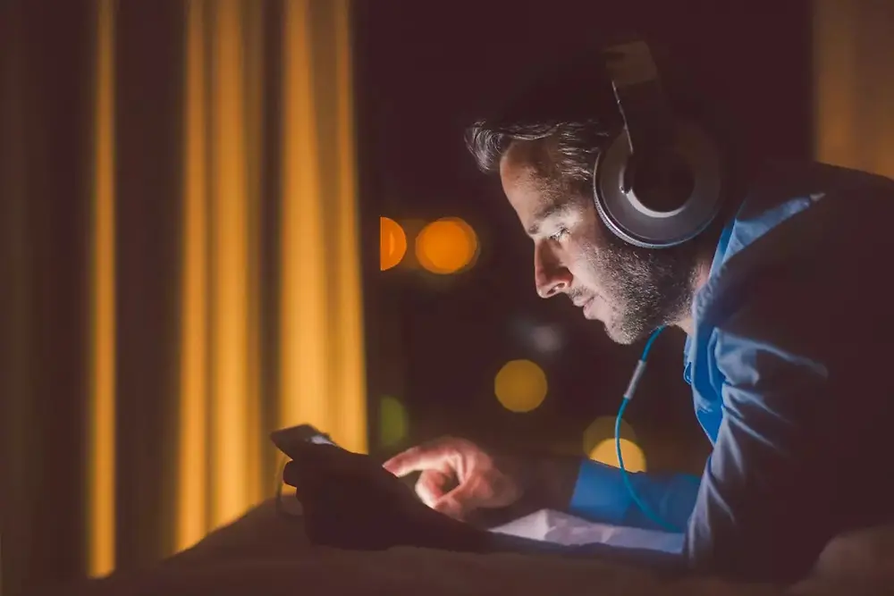 Person nutzt ein Smartphone in einem schwach beleuchteten Raum mit warmem Licht.