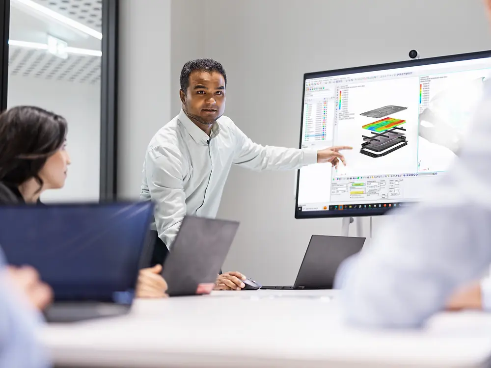 Ein Team arbeitet gemeinsam an Innovationen mit Loctite-Lösungen. Während eines technischen Meetings präsentiert eine Person Modellierungs- und Simulationsdesigns auf einem großen Bildschirm.