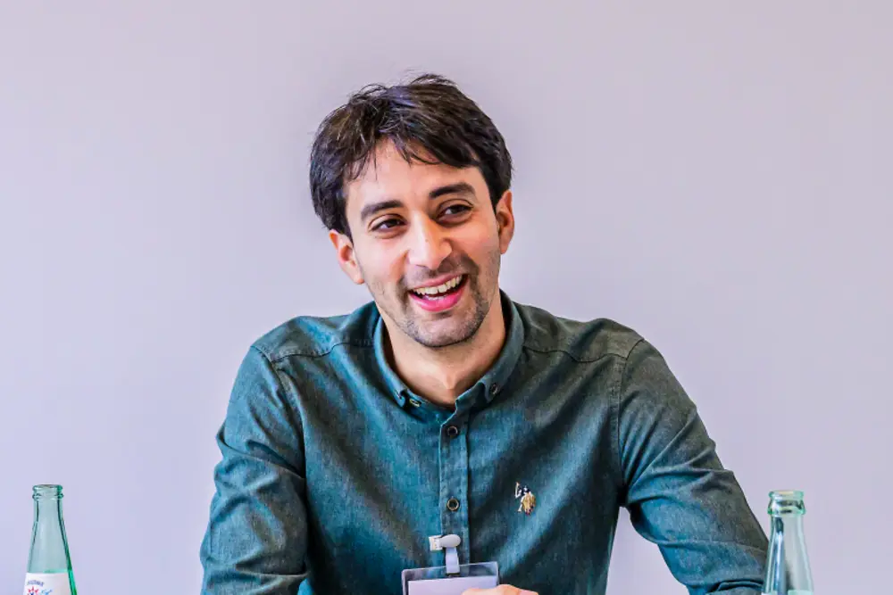 Senior Leader in einem professionellen Meeting-Umfeld während einer Strategiesitzung bei Henkel. Die Person sitzt an einem Tisch mit Dokumenten im Gespräch mit anderen Teilnehmenden.