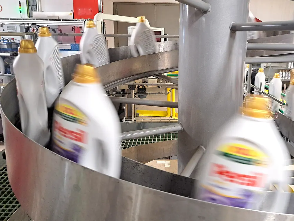 Persil-Waschmittelflaschen bewegen sich mit hoher Geschwindigkeit auf einem gebogenen Förderband.