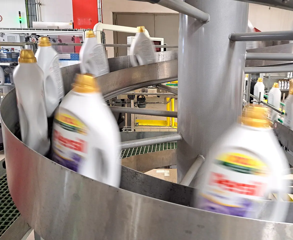 Persil-Waschmittelflaschen bewegen sich mit hoher Geschwindigkeit auf einem gebogenen Förderband.