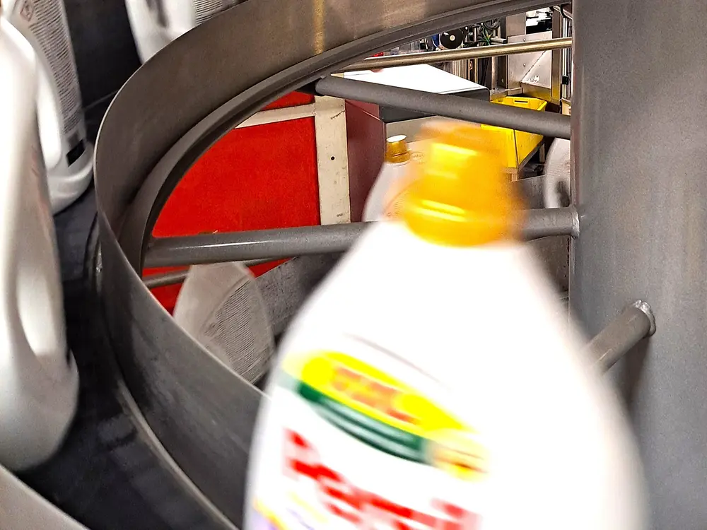 Nahaufnahme einer Persil-Waschmittelflasche auf einem gebogenen Förderband.