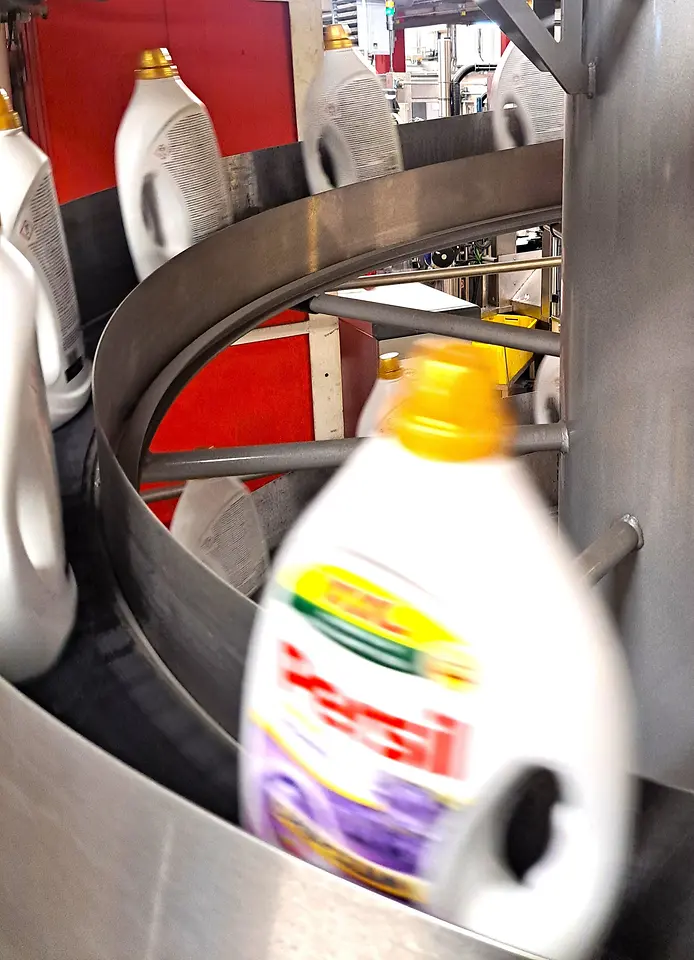 Nahaufnahme einer Persil-Waschmittelflasche auf einem gebogenen Förderband.