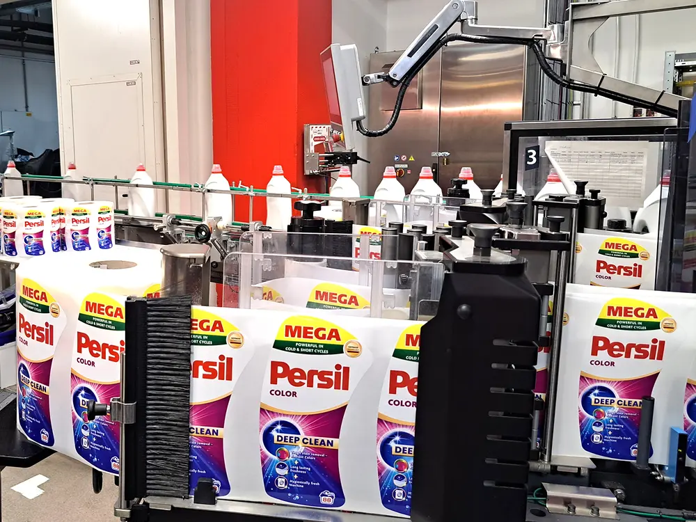 Mehrere Persil-Waschmittelflaschen am Ende der Produktionslinie auf einem Förderband gruppiert.