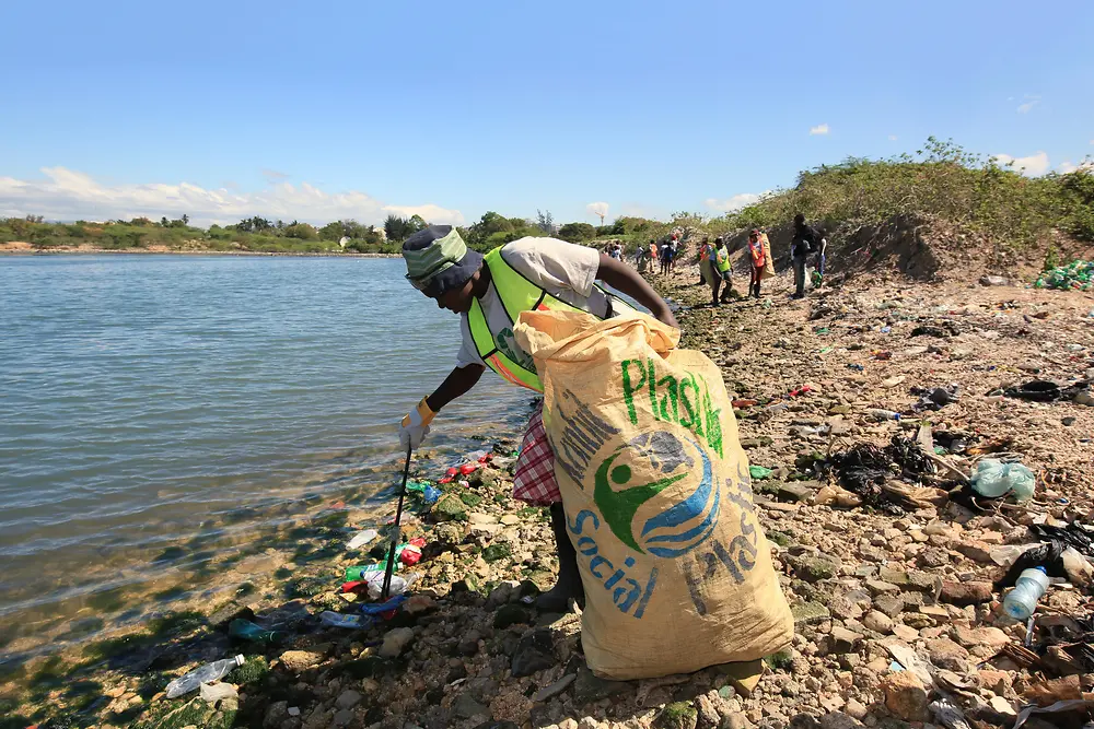 Ein Frau liest in Haiti Plastikmüll am Strand auf